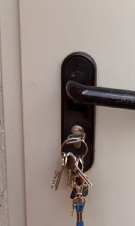 Vit ytterdörr med svart handtag, där nyckelknippan sitter i dörrlåset.